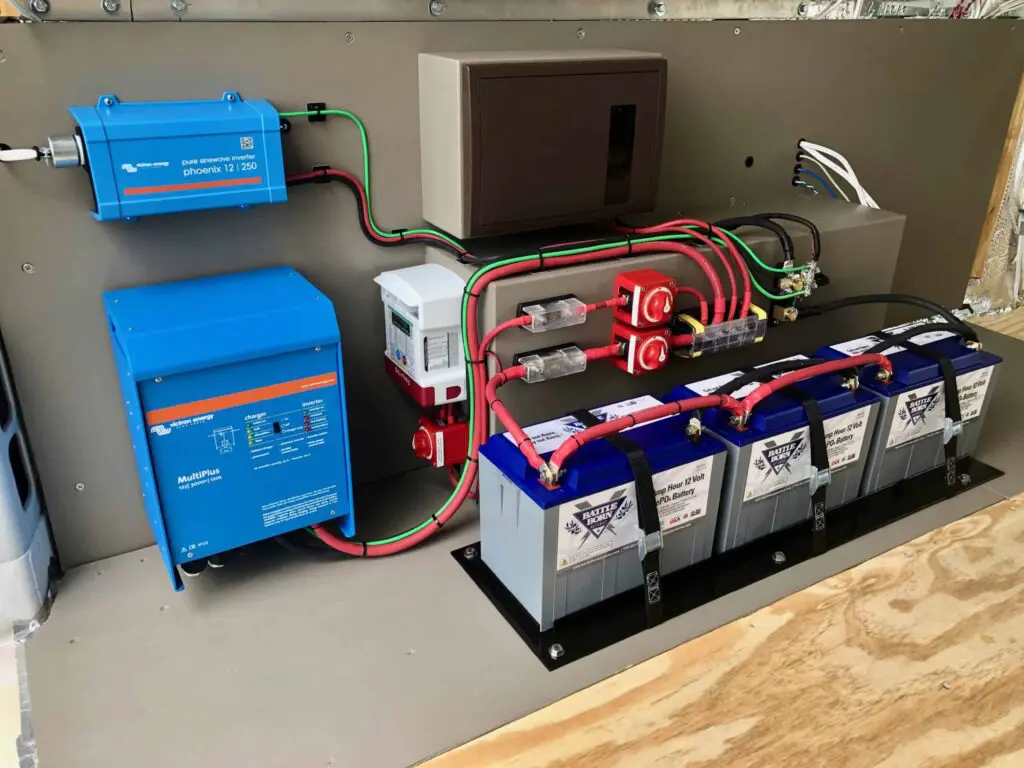 A shot of a vehicle's power system, showing blue Victron Energy components, red battery cut-off switches, and four gray Battle Born LiFePO4 batteries neatly installed.