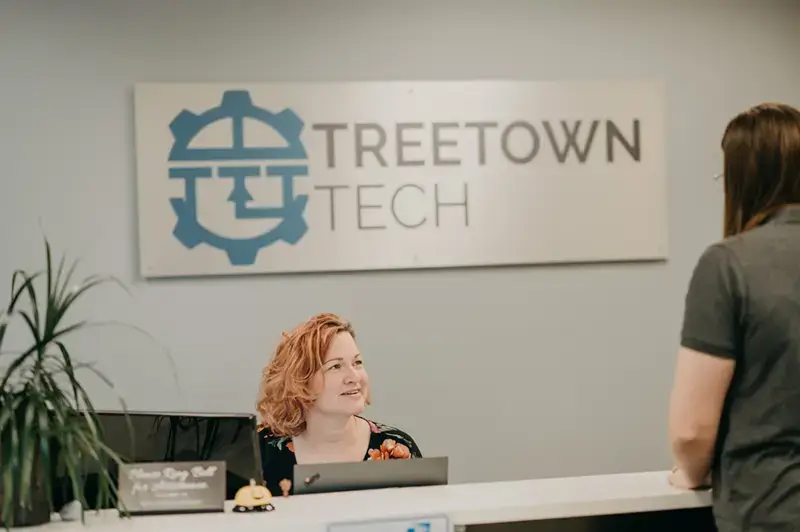 Two Treetown Tech employees having a conversation with a Treetown Tech logo sign in the background.