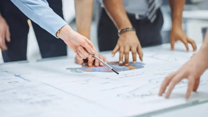 Downloaded Industrial Engineering Facility: Close-up on Hands of Group of Engineers, Technicians and Specialists on a Meeting, Tracing Lines and Analysing Engine Design Technical Drafts Laying on the Table