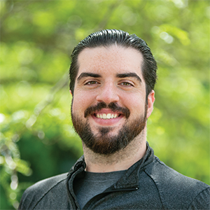 Professional headshot of Jason Bazylewicz, wearing a dark polo, standing in front of a leafy background