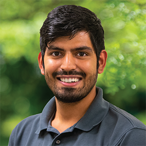 Professional headshot of engineer Parth Patel, wearing a dark gray polo, standing in front of a leafy background